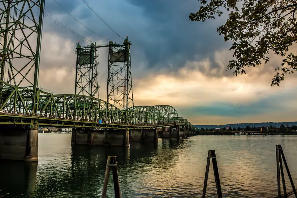 Green metal bridge over Columbia River between Oregon and Washington against cloudy sky.